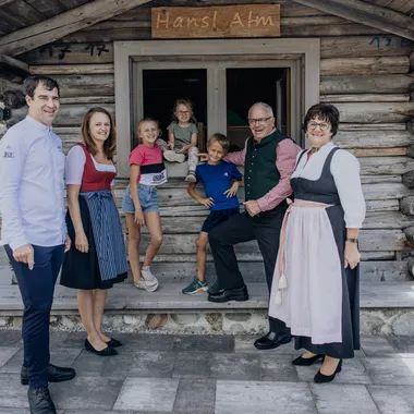 Unternehmenswerte Riederalm Familie in Tracht lächelt vor rustikaler Holz-Almhütte Hansl Alm